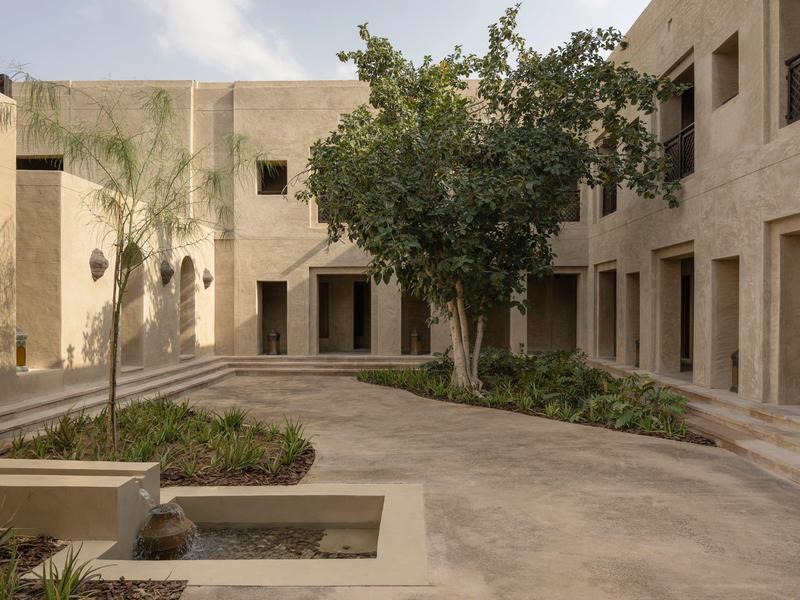 Hotel courtyard with trees, sandstone walls, and a curved pathway.