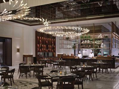 Moderner Restaurantraum mit eleganter Beleuchtung, Holztischen und Stühlen, hellem Marmorboden.