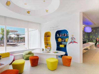 Heller, moderner Kinderbereich mit bunten Sitzmöbeln, Spieltisch und großen Fenstern zur Außenansicht.