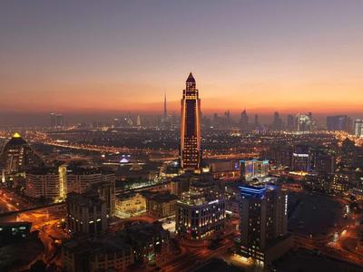 Stadt bei Dämmerung mit hohem Turm, beleuchteten Straßen und weitem Horizont mit Gebäuden.