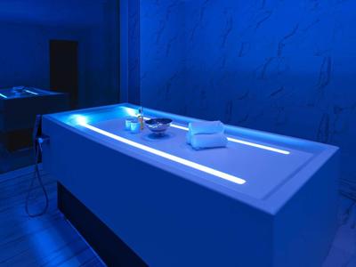 Behandlungsraum mit beleuchtetem weißem Behandlungstisch und blauer Wandbeleuchtung.