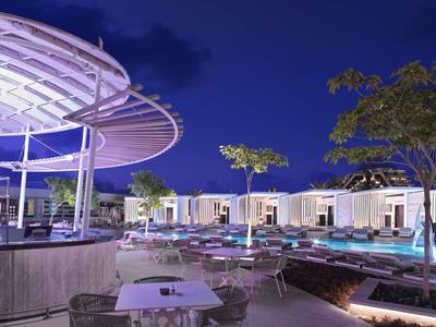 Moderne Außenbar mit weißen Tischen, Pool und moderner Beleuchtung bei Nacht.