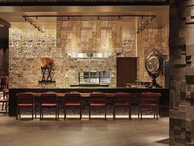 Moderner Barbereich mit dunklem Holz, roten Barhockern und warmen, gedämpften Lichtakzenten.