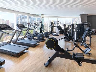 Nowoczesna siłownia z bieżniami, ergometrem wioślarskim i sprzętem siłowym na drewnianej podłodze.