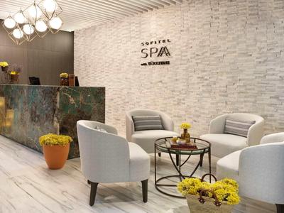 Moderner Spa-Wartebereich mit weißen Sesseln, rundem Tisch, Pflanzen und hellem Steinwand-Design.