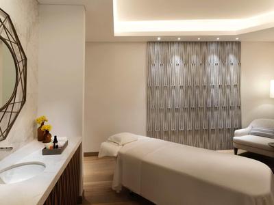 Helles, modernes Spa-Zimmer mit Behandlungsliege, rundem Spiegel und gemütlichem Sessel.