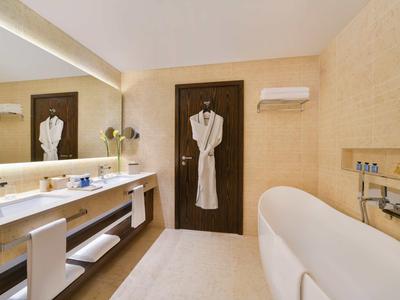 Helles Badezimmer mit weißer Badewanne, großem Spiegel, Waschbecken und Bademantel an dunkler Tür.