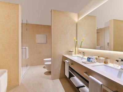 Helles Bad mit beige Fliesen, Doppelwaschbecken, großer Spiegel und moderner Dusche.