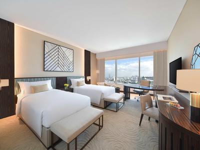 Modernes Hotelzimmer mit zwei Betten, Schreibtisch, großen Fenstern und minimalistischem Design.