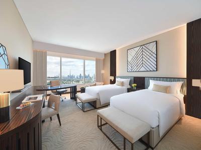 Hell eingerichtetes Hotelzimmer mit zwei Betten, Schreibtisch, Fernseher und großem Fenster mit Stadtblick.