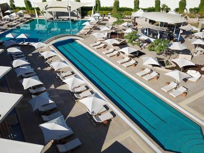 Großer moderner Außenpool mit Liegestühlen, Sonnenschirmen und umliegender Terrasse bei Tageslicht.