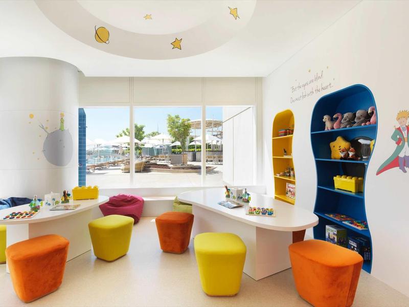 Bunte Sitzhocker und Regale in einem hellen, freundlichen Kinderraum mit großen Fenstern.