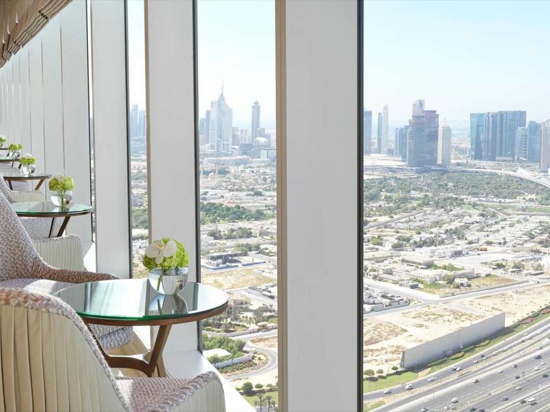 Moderner Sitzbereich mit weißen Sesseln und Glasfenstern, die eine Stadt- und Autobahnsicht bieten.