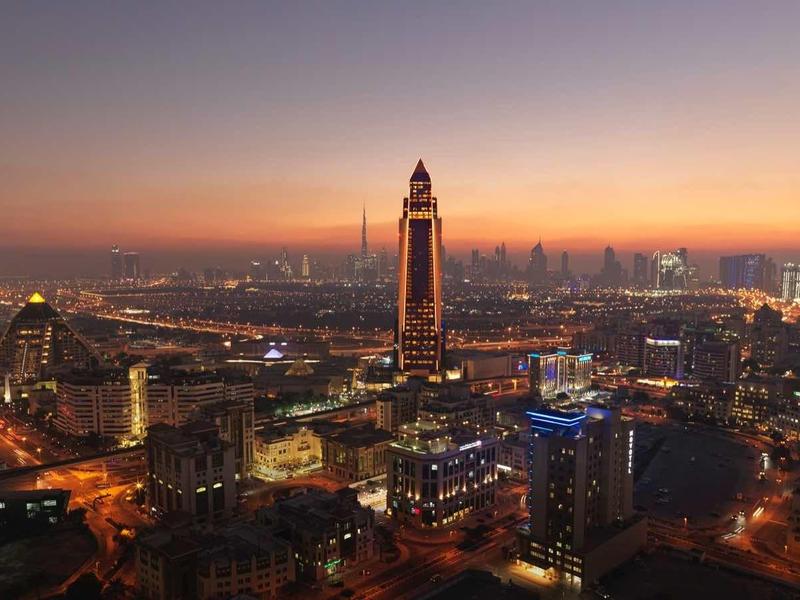Stadt bei Dämmerung mit hohem Turm, beleuchteten Straßen und weitem Horizont mit Gebäuden.