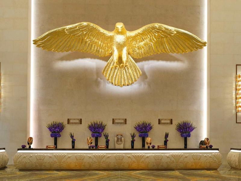 Große goldene Adler-Skulptur an heller Wand über Theke mit Vasen und Blumendekor in elegantem Raum.