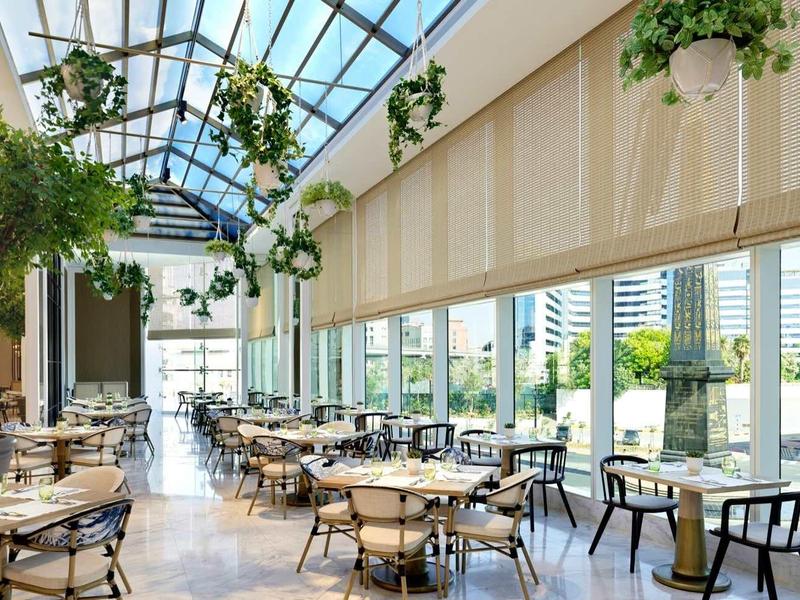 Helles, modernes Restaurant mit großen Fenstern, Pflanzen und vielen Tischen und Stühlen.