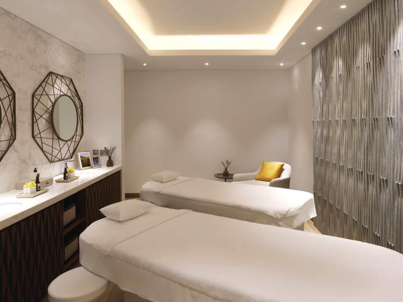 Helles, modernes Wellnesszimmer mit zwei Massageliegen, runden Spiegeln und gedämpfter Beleuchtung.