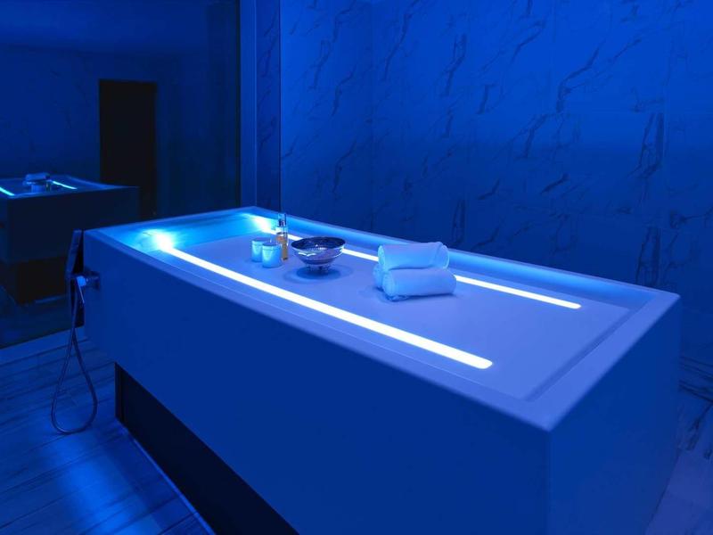 Behandlungsraum mit beleuchtetem weißem Behandlungstisch und blauer Wandbeleuchtung.