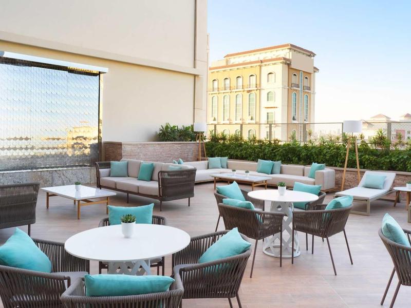 Dachterrasse mit runden Tischen, Stühlen mit blauen Kissen und einer Aussicht auf Gebäude.