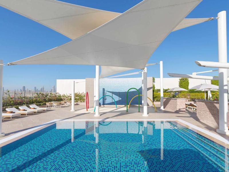 Moderner Pool mit blauem Wasser, weißen Segeln als Sonnenschutz und Holzboden im Außenbereich.