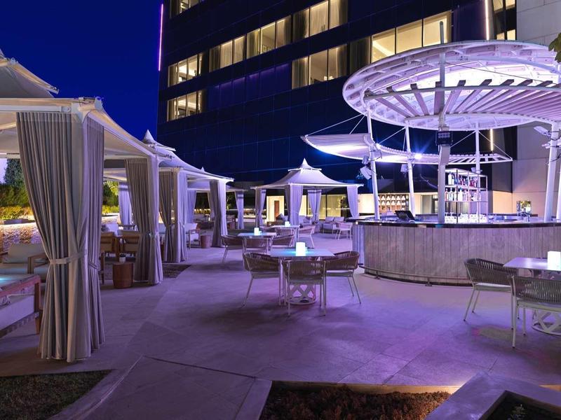 Moderne Terrasse mit runden Sonnenschirmen, Sitzgruppen und beleuchteter Bar bei Nacht.