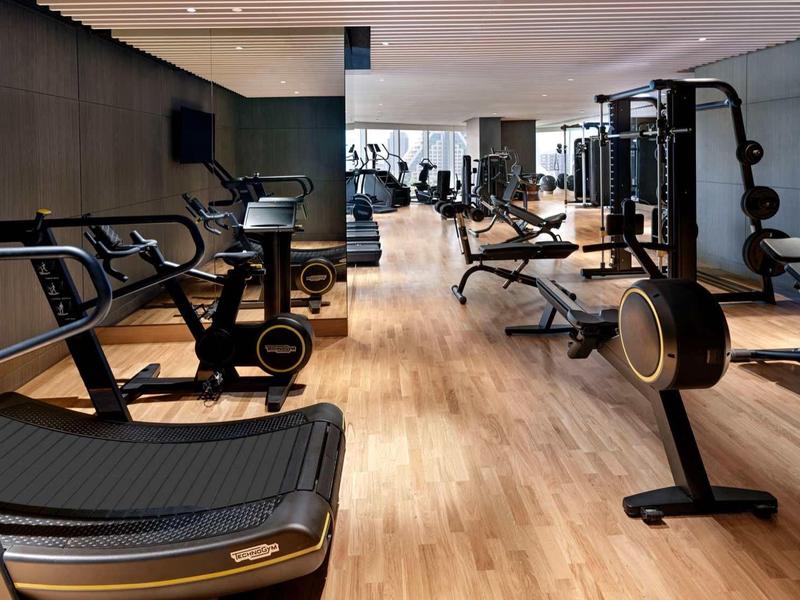 Moderner Fitnessraum mit Holzfußboden, Laufbändern, Kraftgeräten und Spiegeln an der Wand.