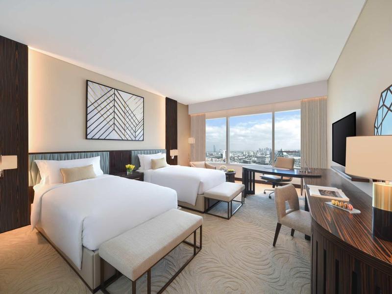 Modernes Hotelzimmer mit zwei Betten, Schreibtisch, großen Fenstern und minimalistischem Design.