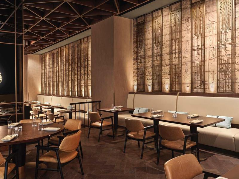 Modernes Restaurant mit Holztischen, braunen Stühlen, Kunstkatze an der Wand und warmem Licht.