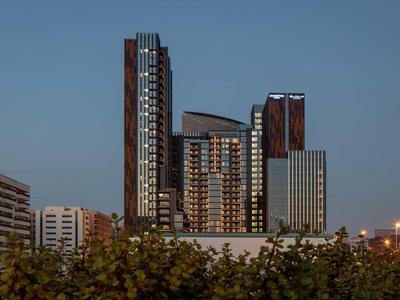 Moderne Hochhäuser mit Glasfassaden bei Dämmerung vor blauem Himmel, unten Grünfläche sichtbar.