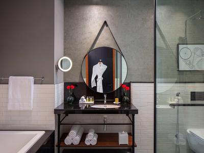 Modernes Badezimmer mit rundem Spiegel, schwarzem Waschtisch, weißen Handtüchern und Glasdusche.