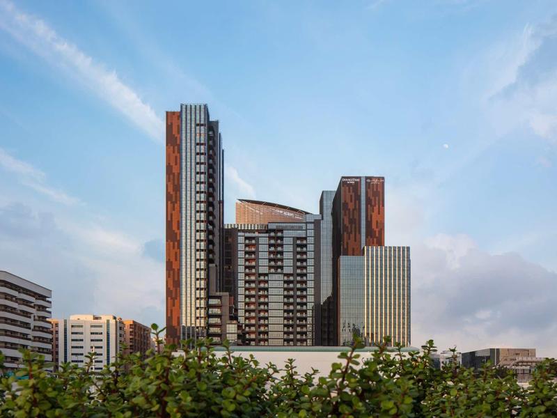 Modern skyscraper with glass and wood facade against blue sky and plants in foreground.