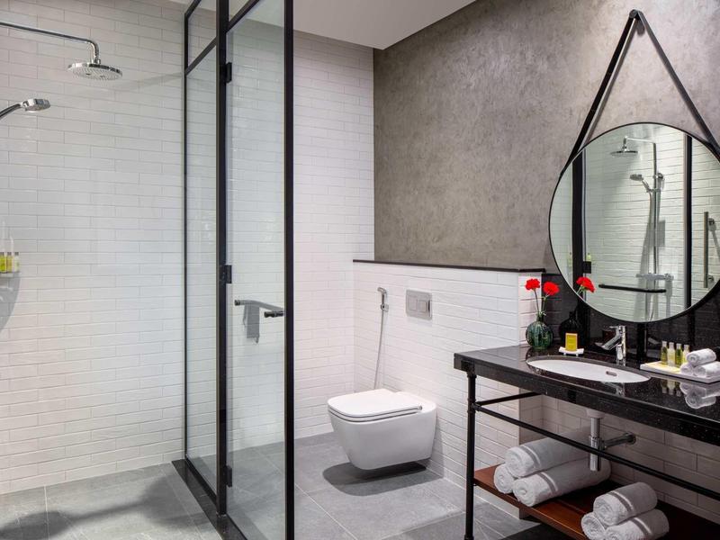 Modern hotel bathroom with shower, toilet, round mirror, and black vanity table.