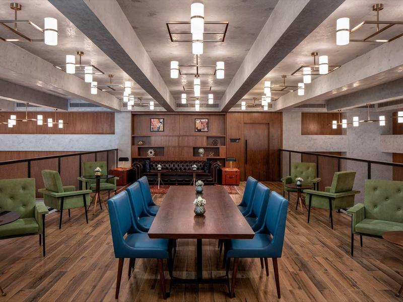 Modern hotel dining area with wooden floor, blue and green chairs, and warm ceiling lights.