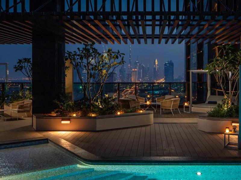 Rooftop terrace with illuminated pool and seating area, night shot with city lights in background.