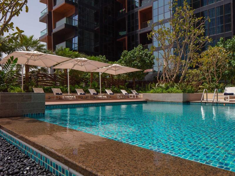 Clear swimming pool beside lounge chairs and shaded umbrellas in a hotel setting.