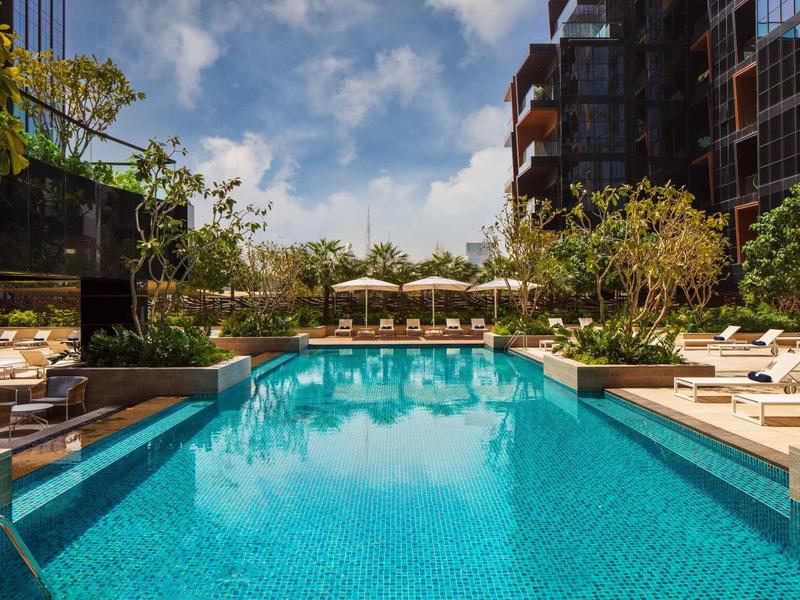 Modern outdoor pool with sun loungers and trees, surrounded by multi-story hotel building.