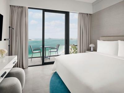 Modernes Hotelzimmer mit großem Bett, Balkon und Meerblick bei Tageslicht.