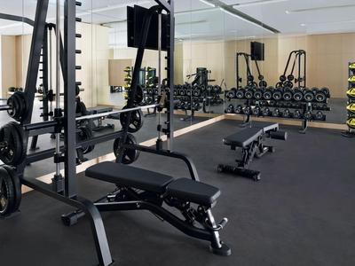 Moderner Fitnessraum mit Gewichten, Hanteln und Trainingsbanken in neutralem Interieur.