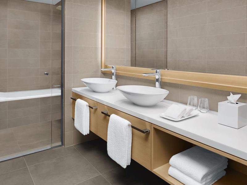 Modernes Badezimmer mit zwei weißen Aufsatzwaschbecken, großem Spiegel und Badewanne mit Glasabtrennung.