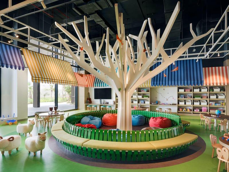 Moderner, bunter Kinderraum mit Baum-Skulptur, bunten Sitzkissen und Tierfiguren aus Holz.