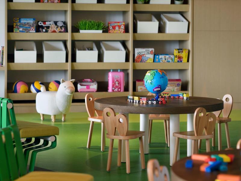 Kindertisch mit Stühlen, Globus und Spielzeug vor Regalen mit Körben und Bällen in hellem Raum.