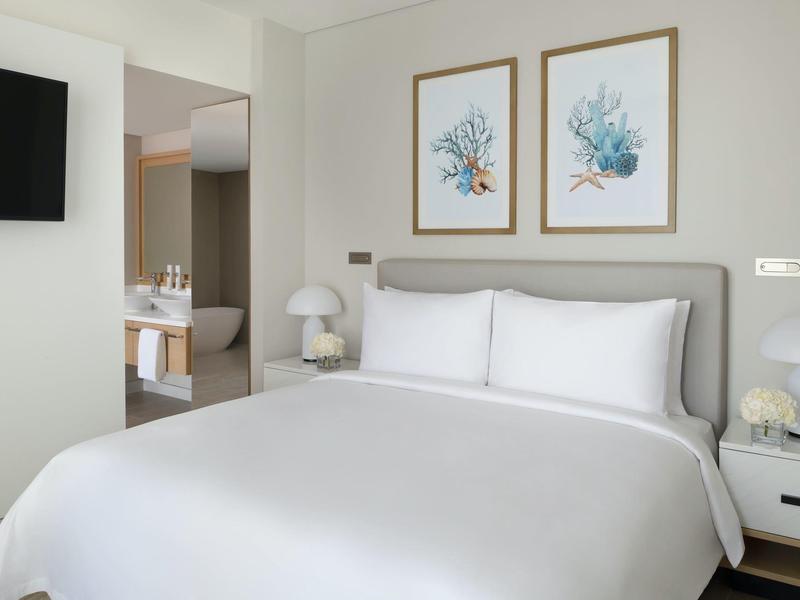 Helles Schlafzimmer mit großem Bett, weißen Bettwäsche, zwei Nachttischen und moderner Wanddekoration.