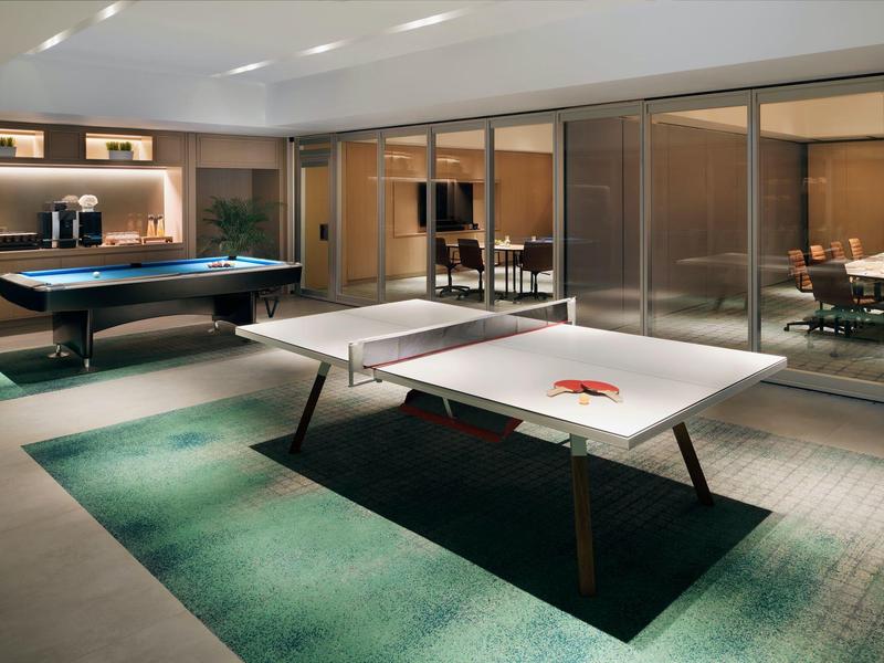 Moderner Spielraum mit Tischtennisplatte, Billardtisch und Glaswänden, dezente Beleuchtung, Teppichboden.