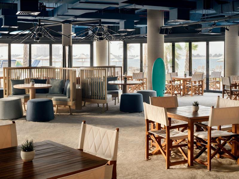 Modernes, helles Restaurant mit Holz- und Polstermöbeln, großen Fenstern und entspannter Atmosphäre.