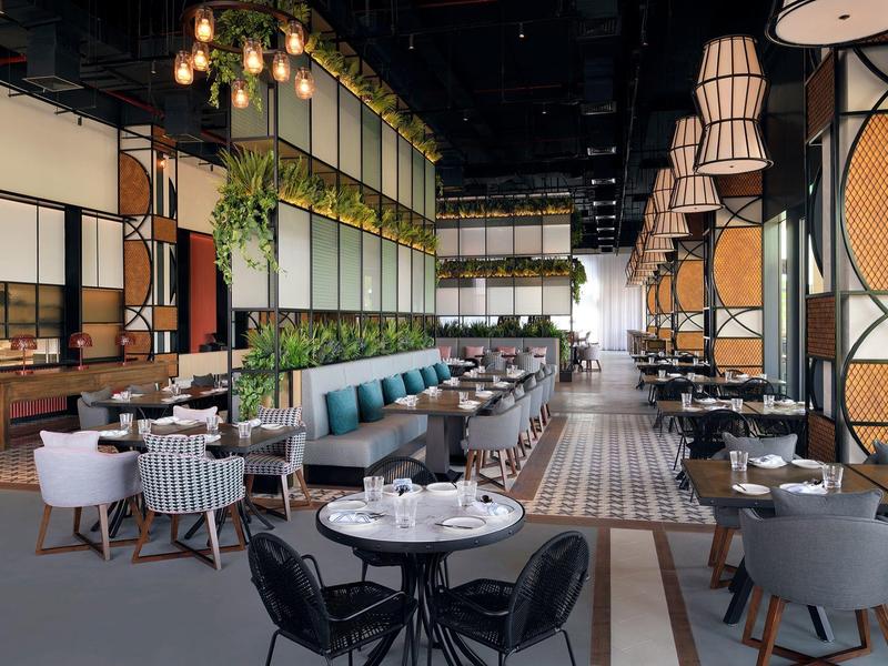 Modernes Restaurant mit großem Gastraum, runden Tischen, grünen Sitzbänken und hängenden Pflanzen.