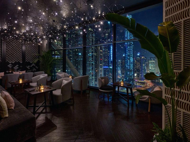 Cozy hotel bar with modern seating areas and panoramic windows overlooking the city at night.