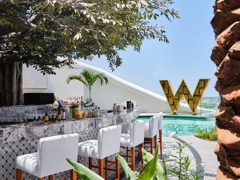 Modern outdoor bar area with white stools next to a pool and a large golden W sculpture