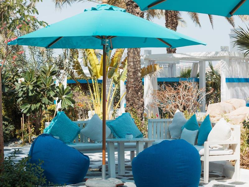 Cozy outdoor lounge with blue bean bags, cushions, and large umbrellas in a tropical setting.