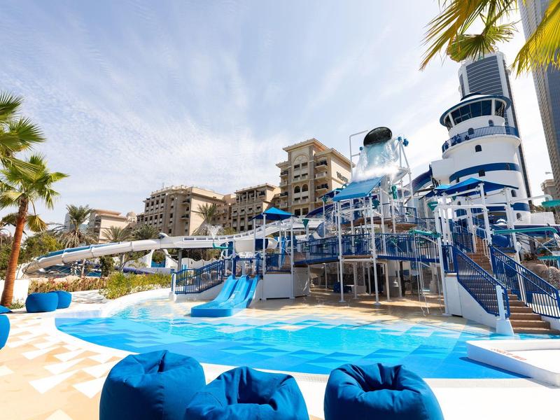Waterpark with slides and pool, surrounded by palm trees and residential buildings.