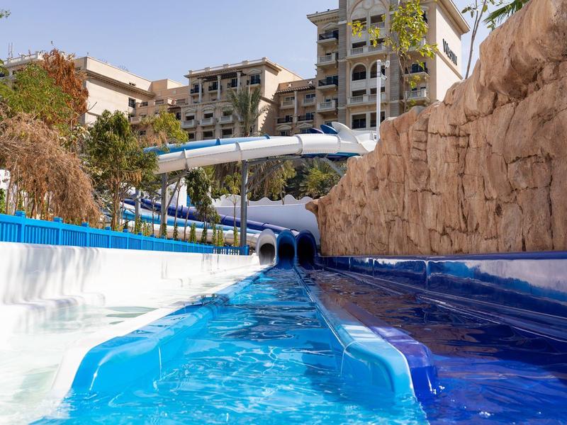 Water park with a calm river slide between rocks and buildings in the background.